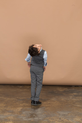 Vista traseira de um menino de terno cinza, dobrando e olhando para a câmera