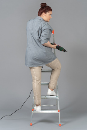 Woman standing on stepladder with a drill