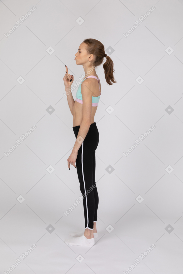Vista lateral de una adolescente en ropa deportiva haciendo gesto de rock