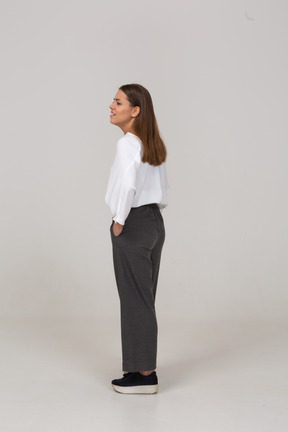 Three-quarter back view of a tired young lady in office clothing putting hands in pockets