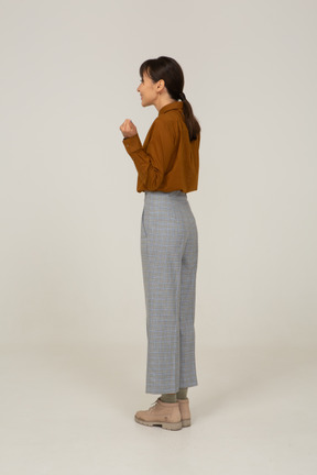 Three-quarter back view of a delighted young asian female in breeches and blouse raising hands