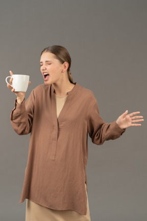 Mujer joven sosteniendo una taza de café y gritando