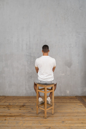 Man sitting on stool with his back toward the camera