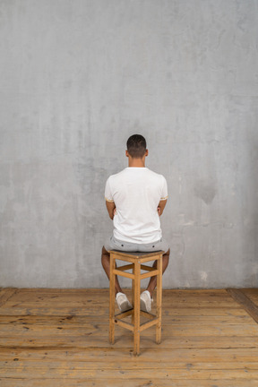 Homme assis sur un tabouret, dos à la caméra