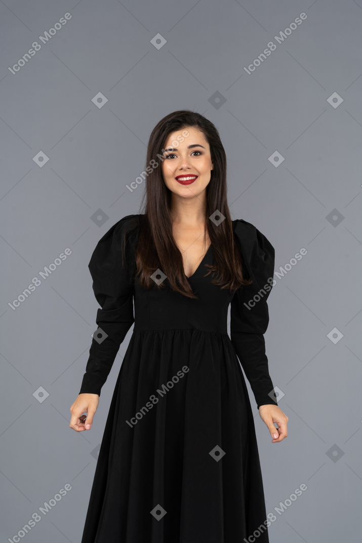 Вид спереди улыбающейся молодой леди в черном платье, стоящей на месте