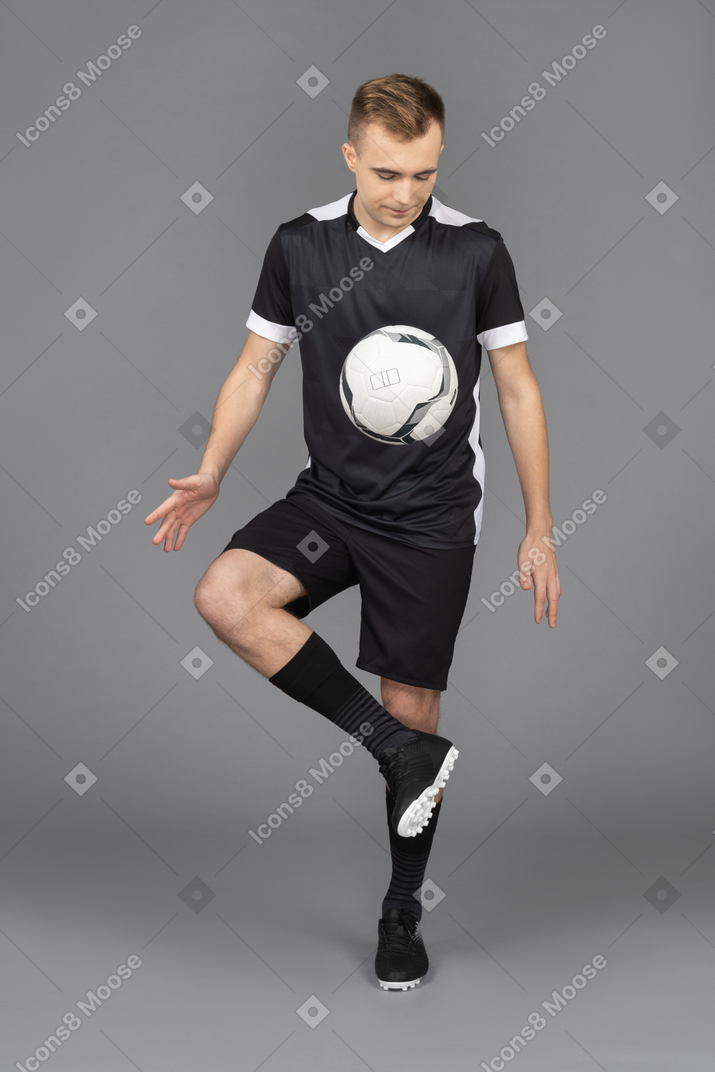 Вид спереди футболиста мужского пола, пинающего мяч и выполняющего трюк
