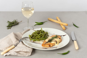 Dish of fish and string beans, glass of white wine, grissini, fork and knife
