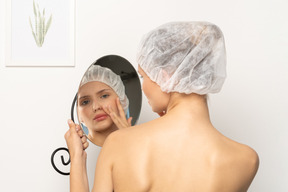 거울에 비친 자신을 바라보는 수술 모자를 쓴 젊은 여성