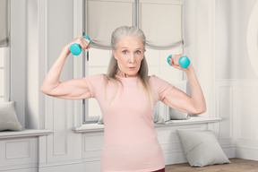 A woman holding two dumbbells in front of her head
