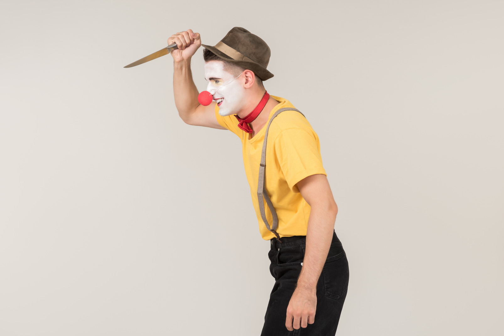 Male clown standing in profile and holding a knife