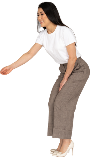 Vista lateral de uma jovem senhora de calça e camiseta esticando a mão e se abaixando