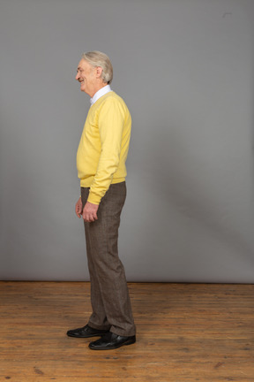 View of a laughing old man wearing yellow pullover and looking aside