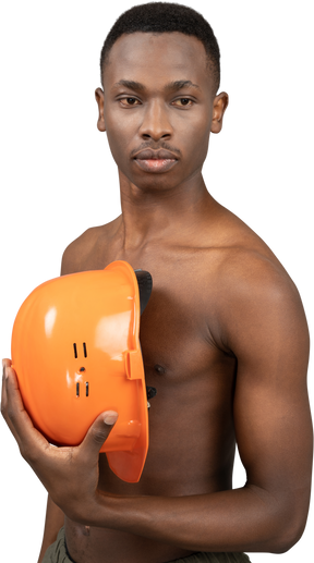 A shirtless young man holding a safety helmet
