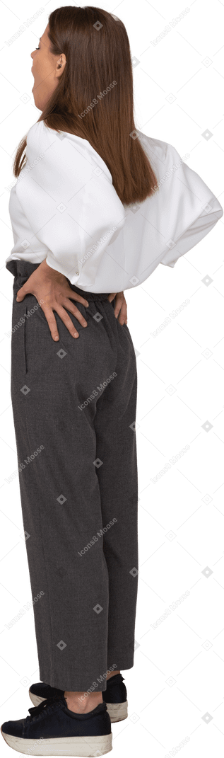 Vista posterior de tres cuartos de una señorita bostezo en ropa de oficina poniendo las manos en las caderas