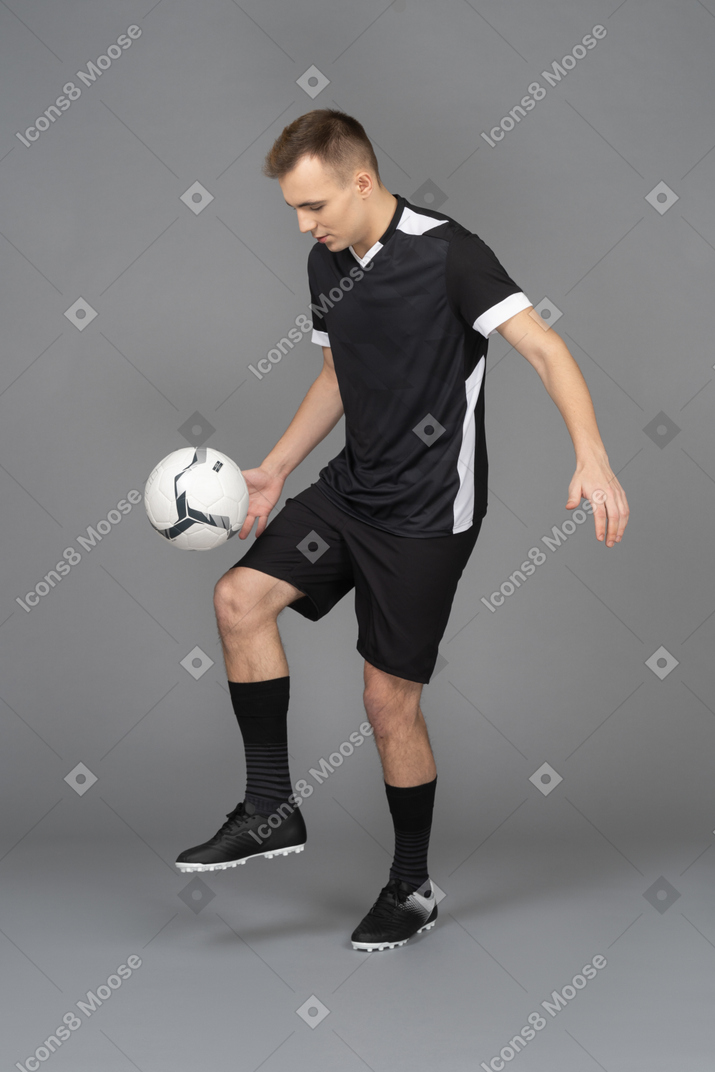 Vista de três quartos de um jogador de futebol masculino chutando uma bola