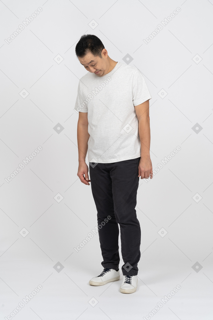 Vista frontal de un hombre con ropa informal de pie con la cabeza inclinada hacia abajo