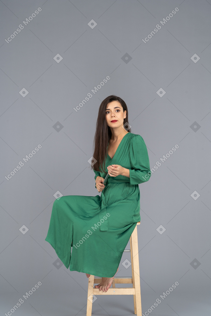 クラリネットを保持しながら椅子に座っている緑のドレスを着た若い女性のフルレングス