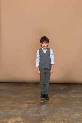 Вид спереди мальчика в костюме, стоящего на месте и смотрящего в камеру