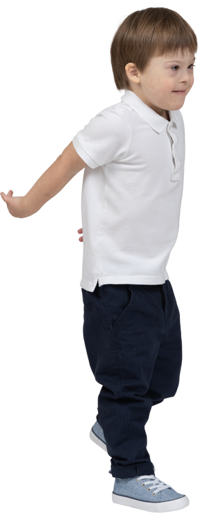 Vista de tres cuartos de un niño dando un paso adelante con las manos detrás de la espalda