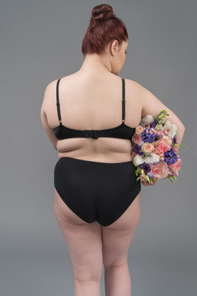 Corpo positivo feminino em lingerie preta posando de volta para a câmera com um buquê de flores