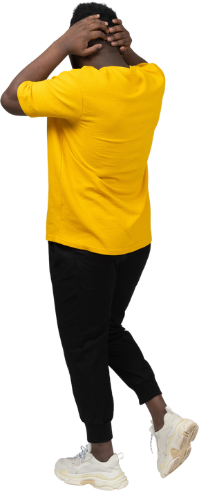 Vista traseira a três quartos de um jovem de pele escura caminhando com uma camiseta amarela tocando a cabeça