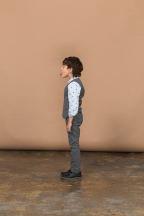 Вид сбоку симпатичного мальчика в костюме, показывающего язык