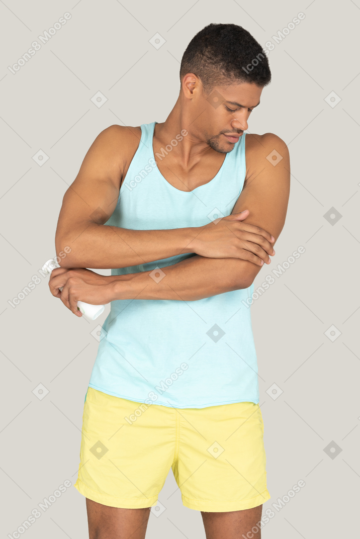 Man in blue tank top and yellow shorts applying cream