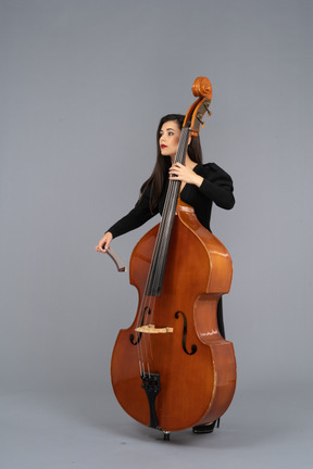 Three-quarter view of a young woman in black dress playing the double-bass with a bow