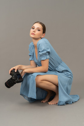 Side view of a young woman in blue dress sitting on a floor with camera