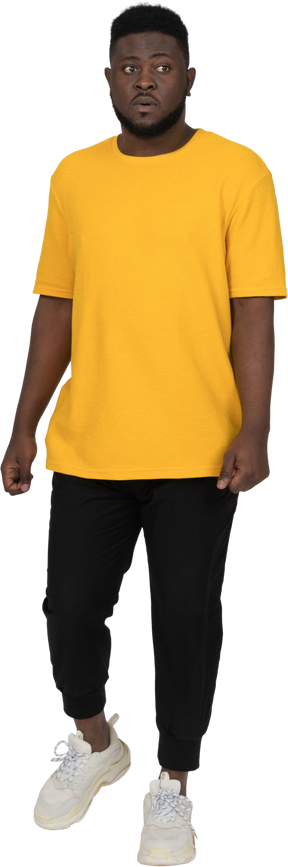 Vista frontale di un perplesso giovane uomo dalla pelle scura in maglietta gialla che guarda da parte