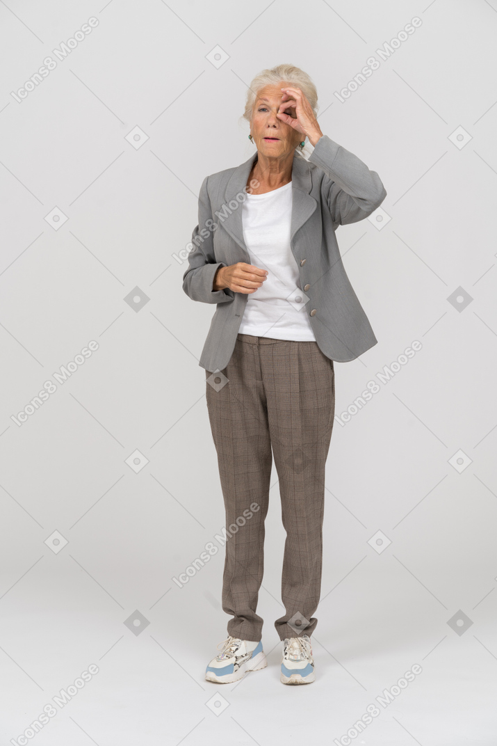 Vista frontal de una anciana en traje mirando a través de los dedos
