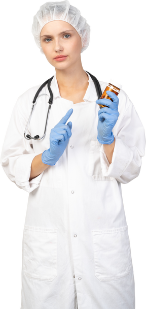 錠剤の瓶に指を指している若い女性医師の正面図