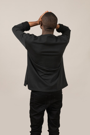 Back view of young man standing with hands on head