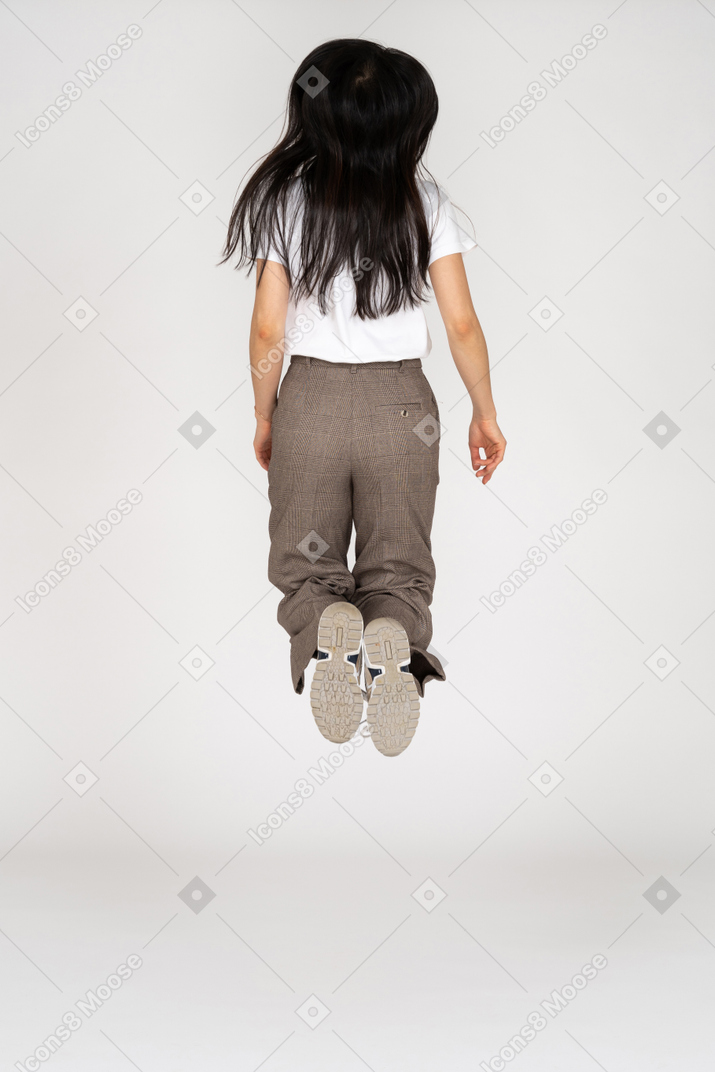 Вид сзади прыгающей молодой леди в бриджах и футболке, сгибающей колени