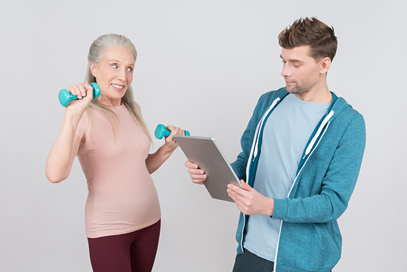Young guy looking on tablet while old woman lifting hand weights