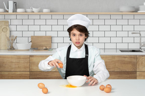 Boy in chef's hat breaking eggs into a bowl