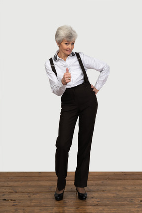 Front view of an old displeased female in office clothes showing a thumb up