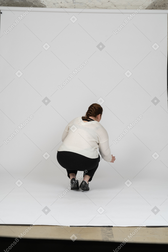 Vista trasera de una mujer de talla grande en suéter blanco en cuclillas