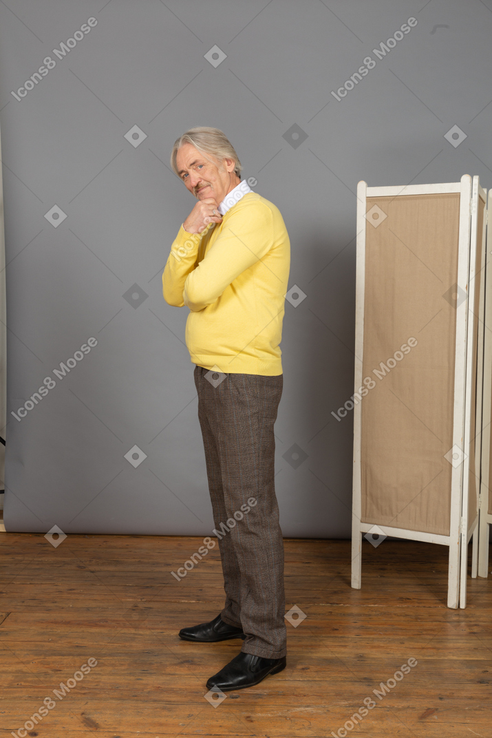 Side view of a thoughtful old man touching chin while looking at camera