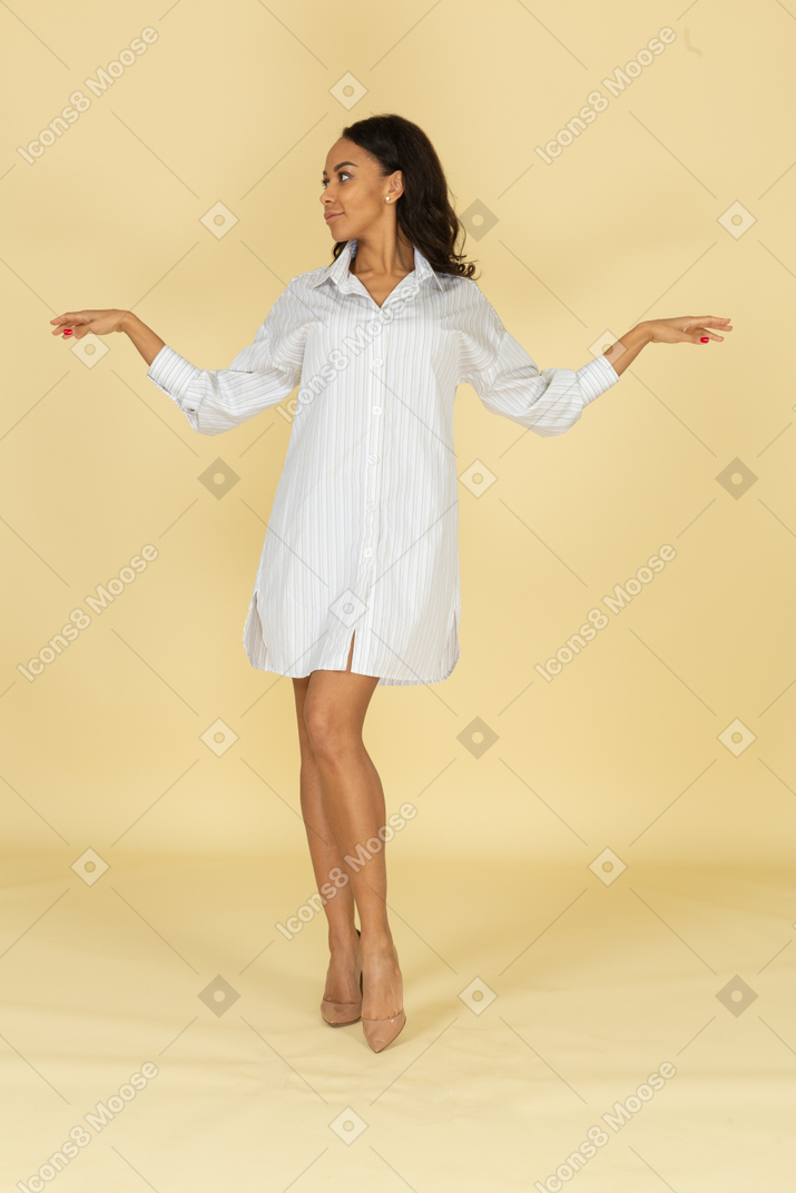 Вид спереди темнокожей молодой женщины в белом платье, протягивающей руки