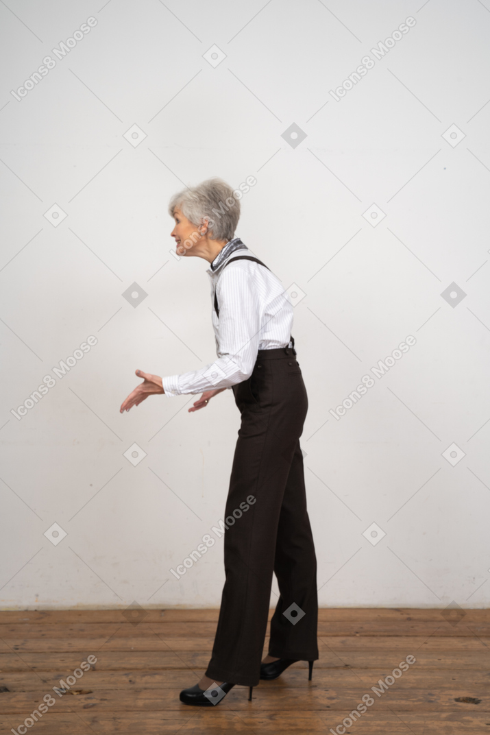 Вид сбоку улыбающейся жестикулирующей старушки в офисной одежде