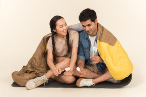 Young interracial couple sitting in sleeping bag and holding marshmallows