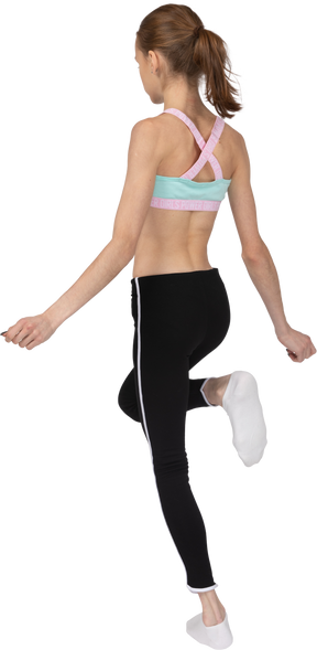 Vista posterior de tres cuartos de una jovencita en ropa deportiva levantando la pierna