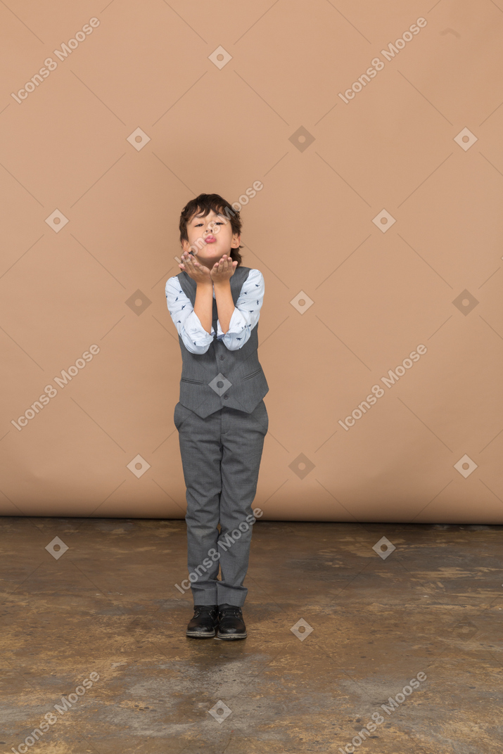 Vista frontal de un niño en traje que sopla un beso