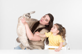 Mom holding ragdoll cat while sitting next to her daughter at the table