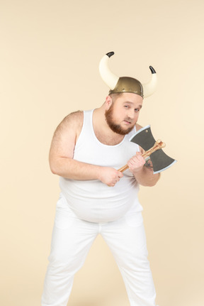 A plus-sized man in white with a horned helmet on his head, holding a double-bladed axe