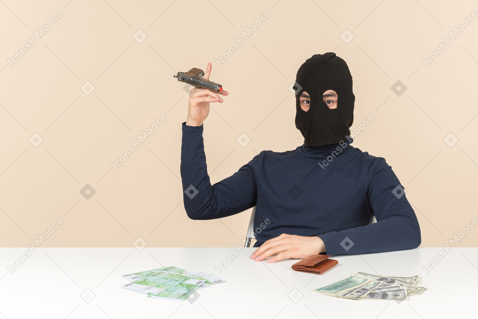 Hacker in balaclava sitting at the table with money bills on it and playing with a gun