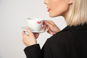 Une photo recadrée d'une jeune femme tenant une tasse de café avec une tache de rouge à lèvres