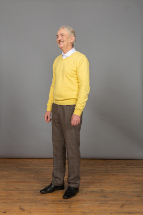 Vista de três quartos de um homem sorridente, vestindo um pulôver amarelo e olhando para o lado