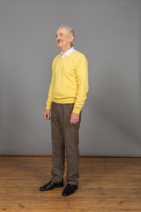 Three-quarter view of a smiling old man wearing yellow pullover and looking aside